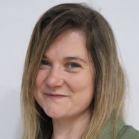 A woman with long, straight, light brown hair smiling at the camera against a plain background.